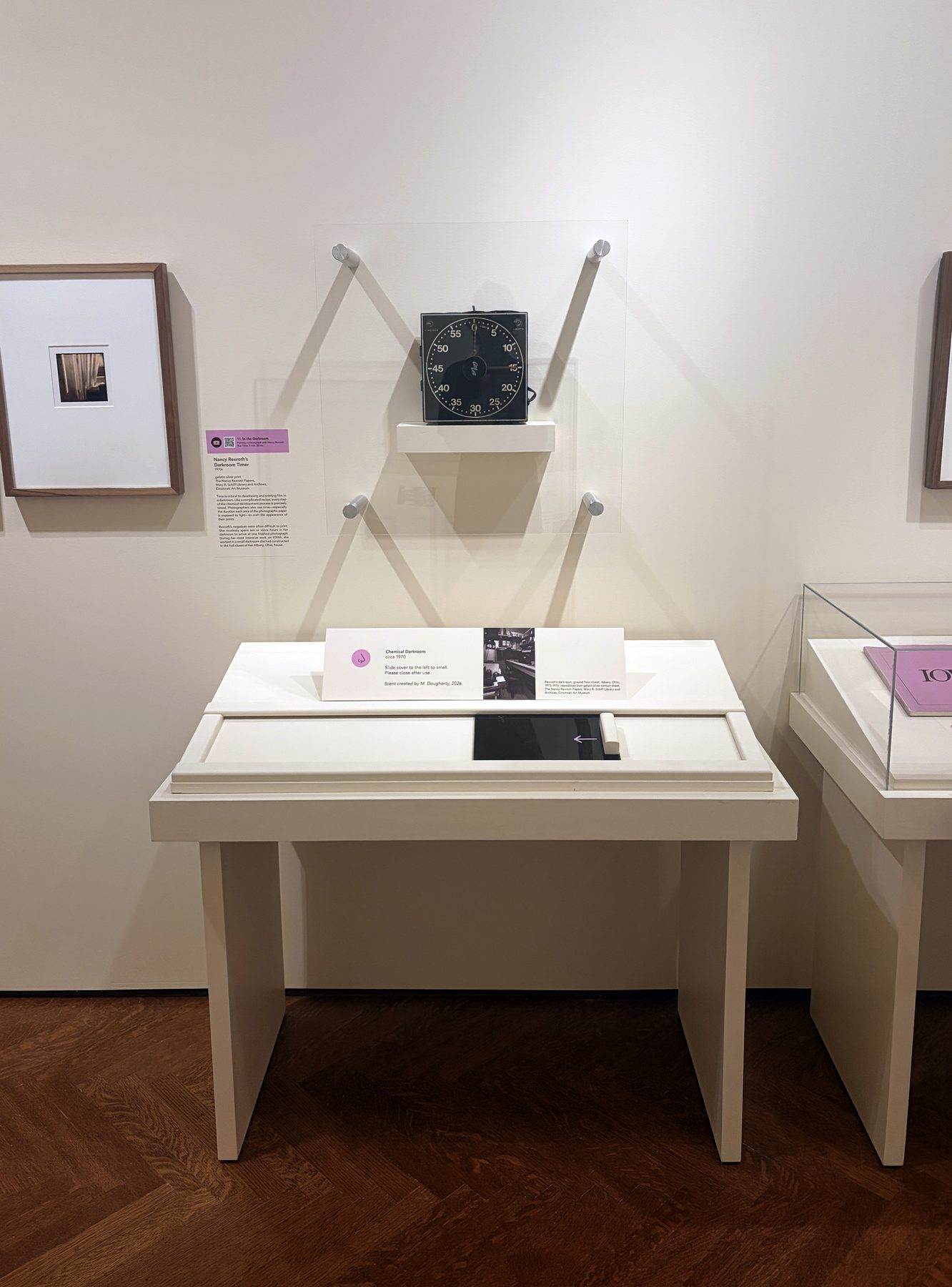 White scent station below Rexroth photographs on a gallery wall, with a label and a sliding cover