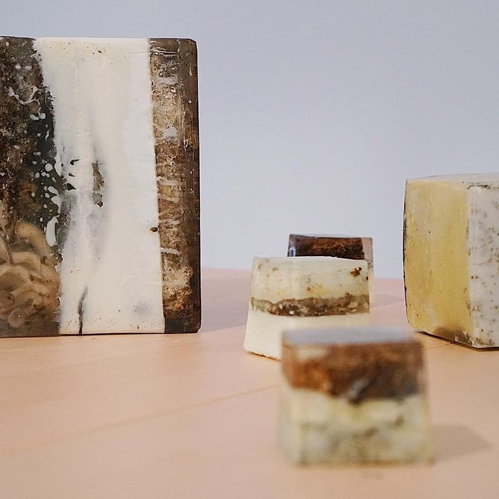 Scented blocks of wax and mycelium on a pale table: a tall slab streaked white and dark, and smaller cubes in front.