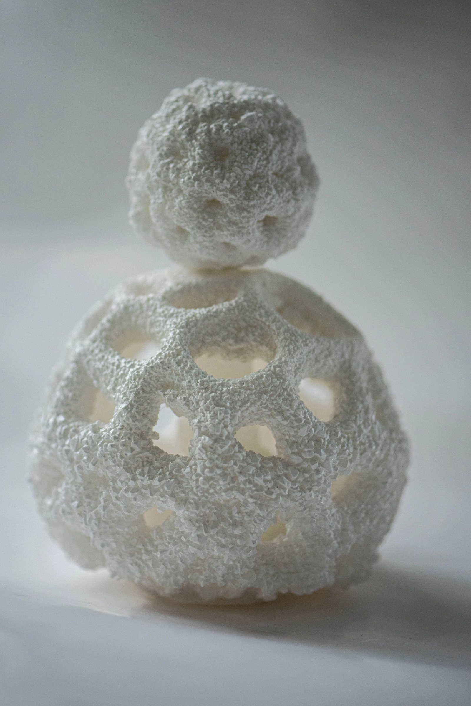 Liminal: a round perfume bottle with a smaller round stopper, its open lattice grown over with white crystals, on a grey ground.