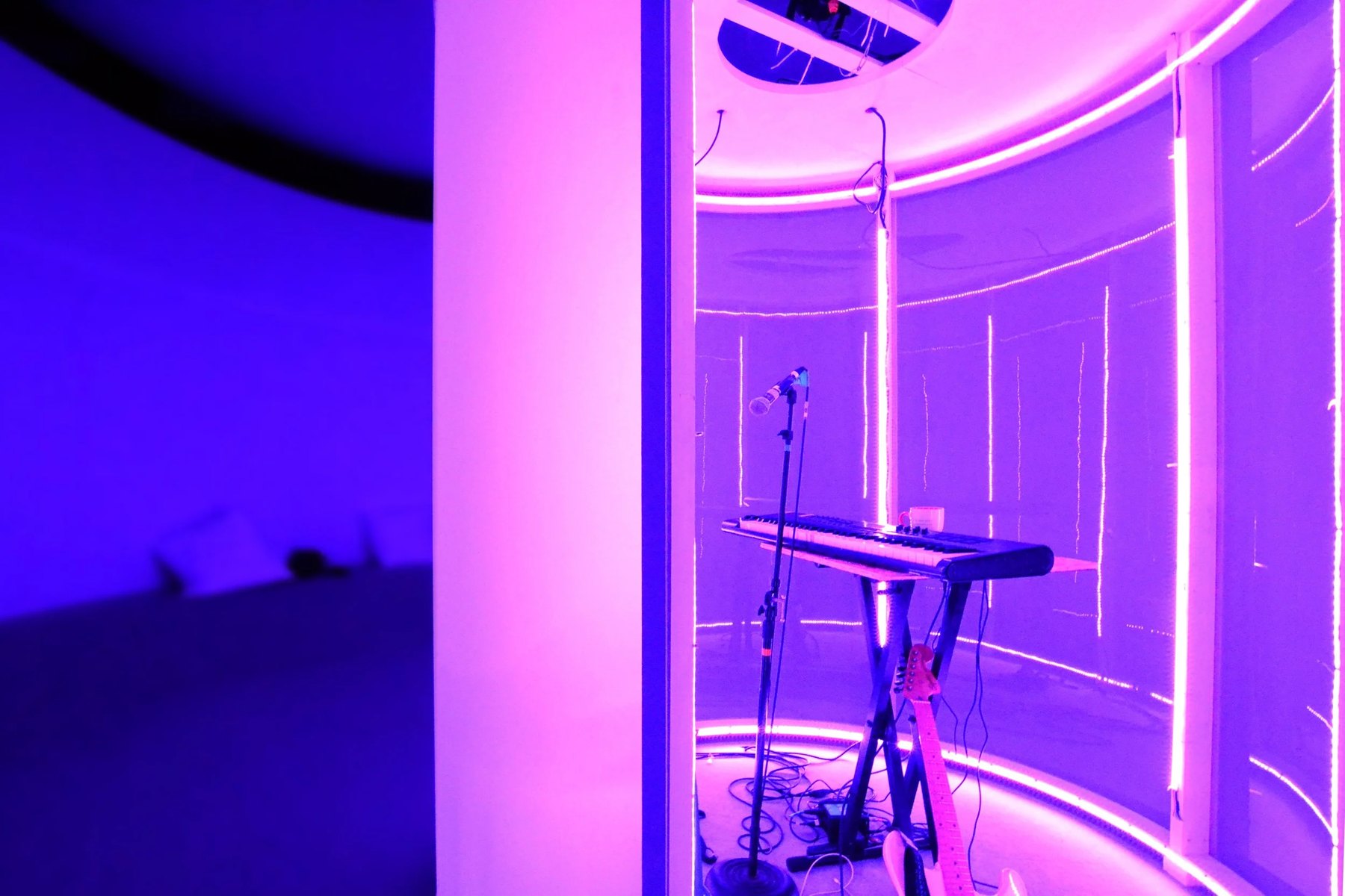Inside the chamber: a keyboard and microphone stand ringed by pink light tubes behind a translucent wall.