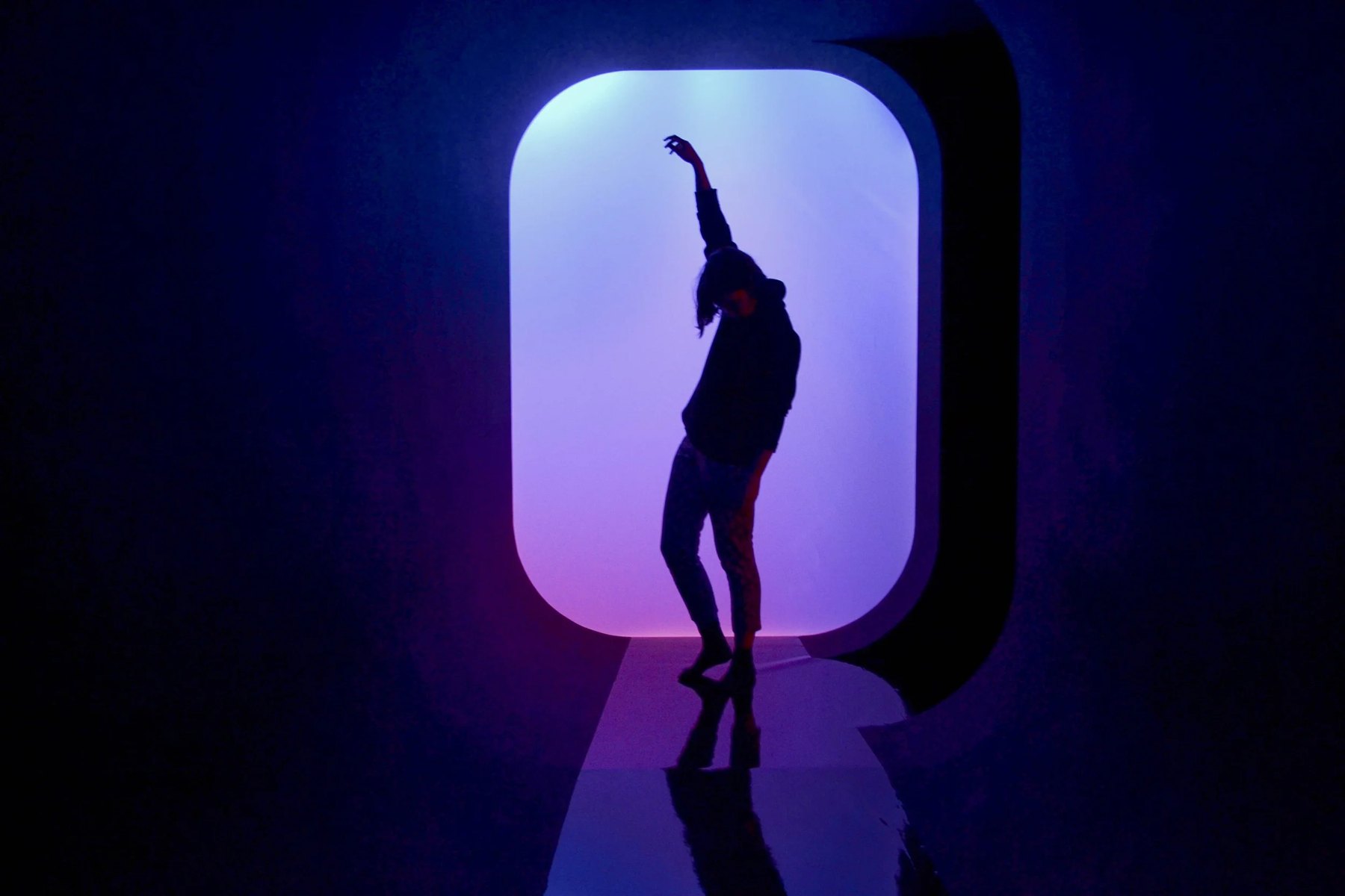 A silhouetted figure dances in a rounded doorway of white and violet light.