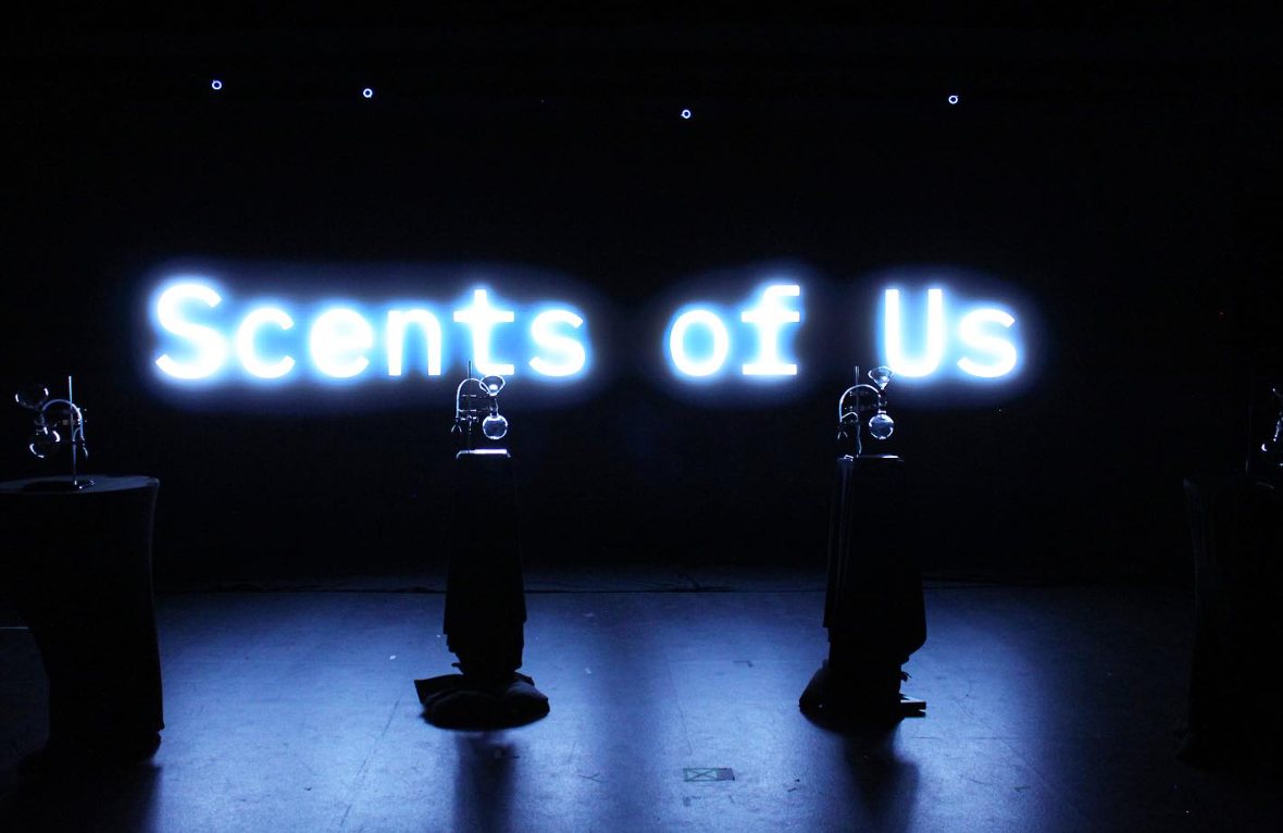 Four pillars topped by glass diffusers before an LED wall that reads Scents of Us.