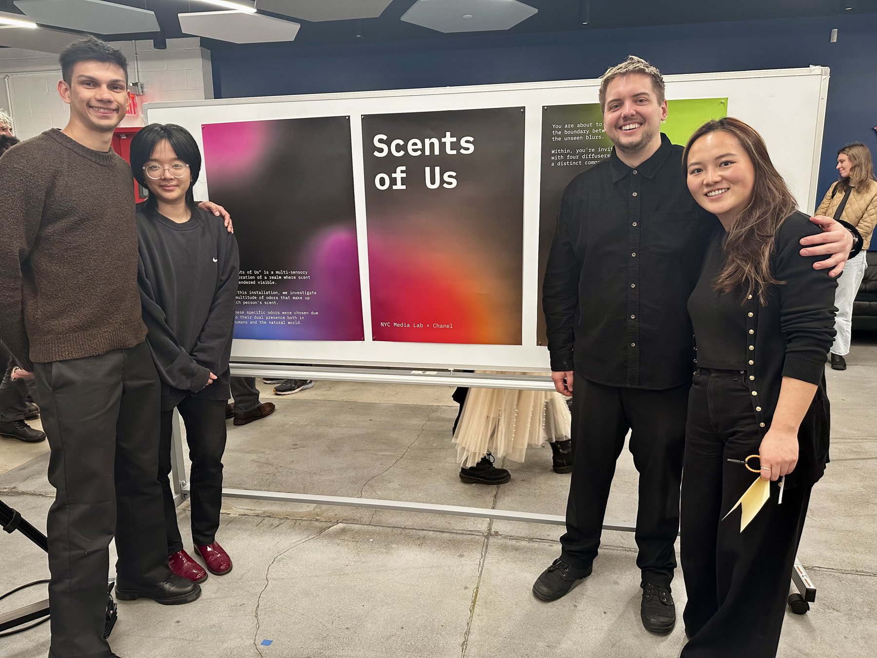 Four members of the team stand in front of the Scents of Us posters at the showcase.